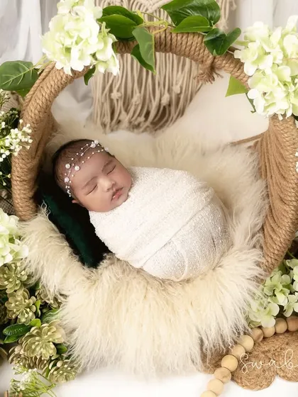 This baby is swaddled in white and nestled in a jute-wrapped basket, surrounded by white hydrangeas and pinecones. The macrame in the background enhances the bohemian theme.