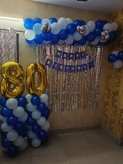 An 80th birthday celebration with a blue and white balloon backdrop and large foil numbers.