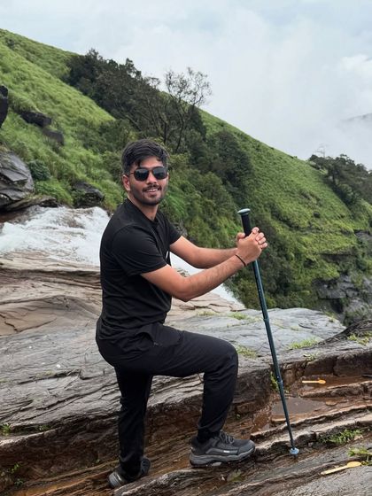 A trekker with a hiking pole poses confidently by the cascading water at Bandaje.