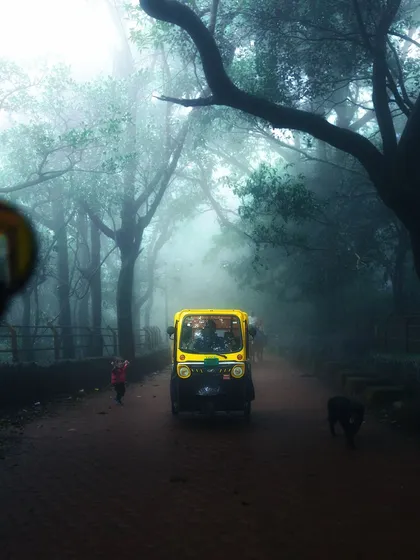A classic yellow auto-rickshaw emerges from the dense fog in Matheran, a scene that feels straight out of a movie.