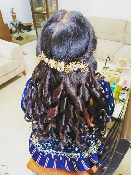 A half-up hairstyle with structured curls, adorned with a golden hair accessory. This is a glamorous look, perfect for a reception or cocktail party.