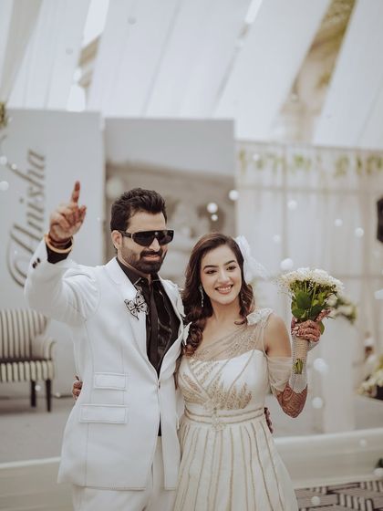 A stylish portrait from the reception. The groom points to the sky in celebration while the bride holds her bouquet, both looking chic and happy, ready to party the night away.