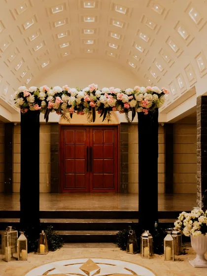 A twilight affair begins with an elegant entrance. A simple floral arch over dark pillars, flanked by lanterns, sets a sophisticated and moody tone for an evening cocktail party.