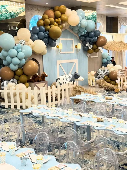 A wide shot of the entire farm party setup, showing the kids' tables in the foreground and the impressive barn backdrop and balloon arch on the stage.