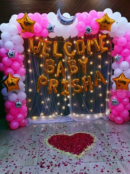 A personalized welcome for baby Prisha. This setup features a fairy light curtain backdrop, a pink and white balloon arch with star foils, and a heart made of rose petals on the floor. It’s a magical way to celebrate her arrival.