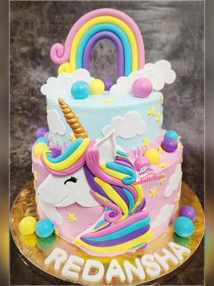 A magical two-tier unicorn cake designed for a fantasy-filled birthday. The bottom tier features a unicorn face with a rainbow mane, while the top tier is a dreamy sky with a fondant rainbow.