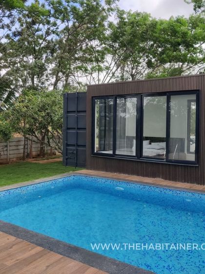 A poolside view of a container home, showcasing the sleek exterior cladding and large windows.