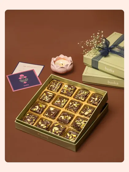 An angled view of a festive sweet box, highlighting the nut-topped chocolates inside. The composition includes a greeting card and a decorative candle to build a complete festive story.