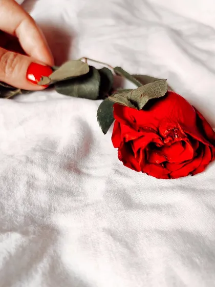 A simple, clean flatlay of a hand with red nail polish holding a single red rose on a white fabric background. Sometimes the most minimal setups can be the most impactful for product or concept photography.