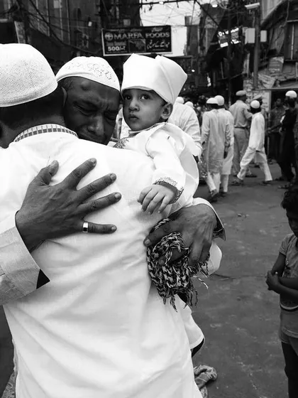 A father holds his son close amidst the crowded streets during Eid, a black and white photograph that focuses on the powerful emotion of their connection.