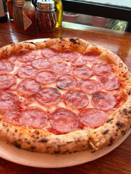 A classic salami pizza, sitting on the table and looking delicious.