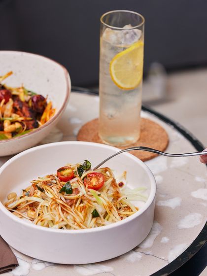 Our vibrant raw papaya salad is a fresh and wholesome option for a light lunch. It's paired here with a glass of our house-made ginger ale for a refreshing and balanced meal.