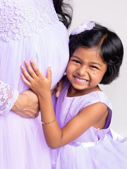A close-up shot capturing the pure excitement of a big sister-to-be. Her joyful grin as she hugs her mom's belly says it all in this heartwarming maternity photo.