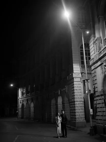 A wide shot of a couple on a deserted city street at night, the single streetlight creating a cinematic and lonely mood.