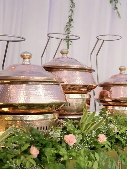 A row of our signature hammered copper chafing dishes, beautifully integrated with arrangements of baby's breath and pink carnations.
