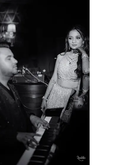 A black-and-white shot that feels like a classic movie scene. The groom at the piano with his bride beside him creates a timelessly romantic image.