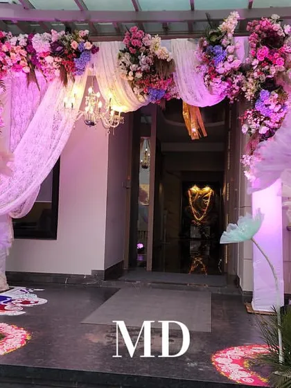 The entrance decor for our pastel Mehendi event. A beautiful arch adorned with pink and purple flowers, draped fabric, and whimsical paper flowers welcomes guests into the celebration.