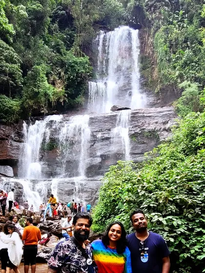 Three friends posing with the majestic Hebbe falls behind them during a Chikmagalur adventure.