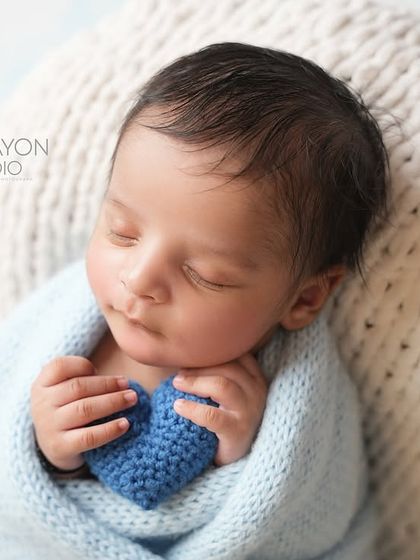 A swaddled newborn holds a small, knitted blue heart, a simple and sweet symbol of the love that surrounds them.