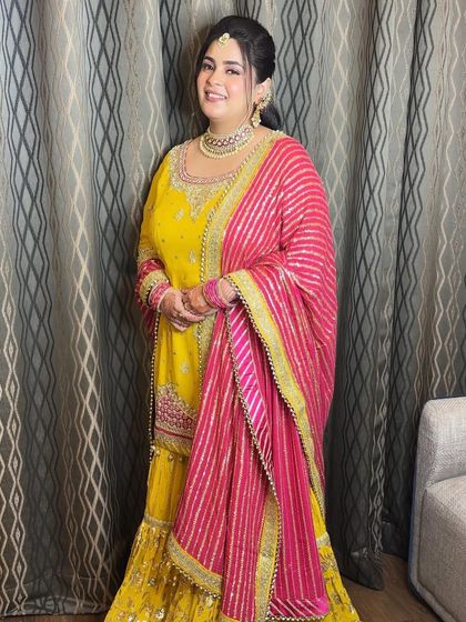 A fresh-faced beauty for her Shagun ceremony. The bright yellow and pink outfit is paired with soft, rosy makeup for a look that is youthful and celebratory.