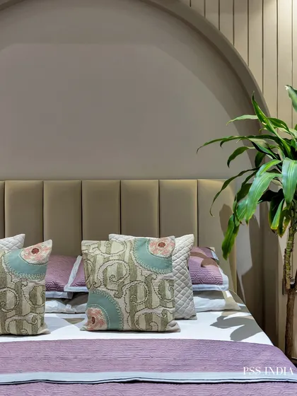 A close-up on the bed in the mauve-toned room, showing the beautiful paisley and patterned cushions that add a layer of intricate detail to the simple, elegant design.