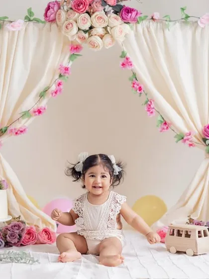 A beautiful smile from the birthday girl in her floral tent. This setup, complete with a cake and soft flowers, is perfect for a classic and elegant first birthday photoshoot for a baby girl.