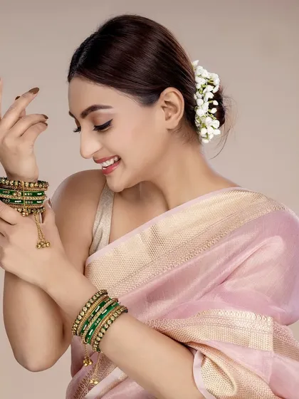 A joyful shot of a model admiring her green and gold traditional bangles. This candid-style photo is great for social media content, creating a relatable and happy brand image.