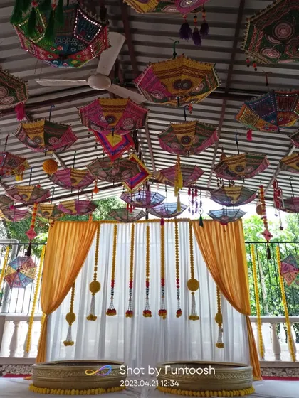 For a vibrant Haldi function, we created this beautiful outdoor setup. The ceiling is decorated with colorful Rajasthani umbrellas, while the backdrop features yellow and white drapes with traditional marigold flower strings.
