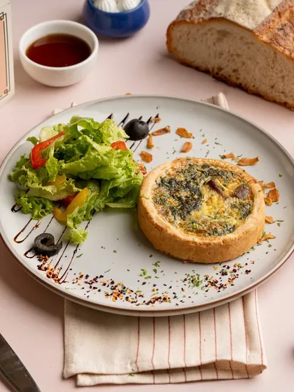 My Creamy Spinach Quiche is a savory delight. It features a buttery, flaky tart crust filled with a rich custard of spinach and cheese, served alongside a fresh side salad.
