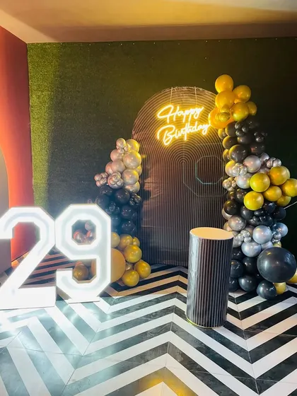 A modern 29th birthday decoration with a geometric-patterned floor. The setup includes a black and yellow balloon arrangement and large light-up numbers.