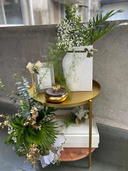 An elegant corporate gift setup. This arrangement on a sleek gold side table features a photo frame, a scented candle, and other curated items, all tied together with fresh greenery for a sophisticated and professional presentation.