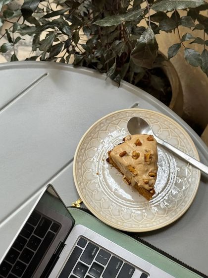 A slice of our comforting winter special carrot cake, enjoyed with a laptop for a cozy work-from-cafe session.
