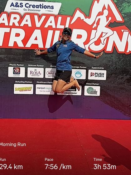 The pure joy of finishing. A runner jumps for joy at the Aravali Trail Run, with her race stats displayed.