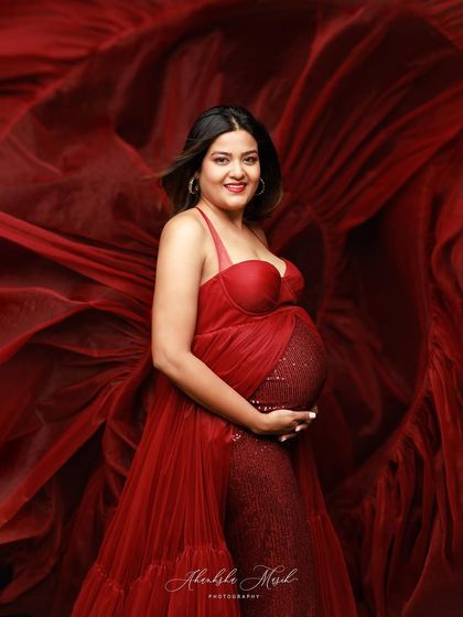 A close-up portrait in a stunning red gown, capturing the joyful smile and radiant glow of the expectant mother.