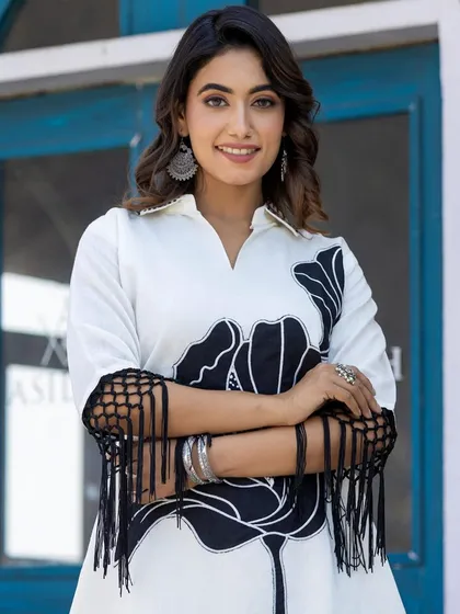 A closer look at the details on the black and white cord set. You can see the intricate black floral appliqué and the stylish fringed detailing on the sleeves, which add a unique, modern touch to the outfit.