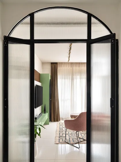 I used a metal and fluted glass partition with a bold arch to create a dramatic entryway into the living room. It separates the space while allowing light to pass through, offering a tantalizing glimpse of the colorful interior.