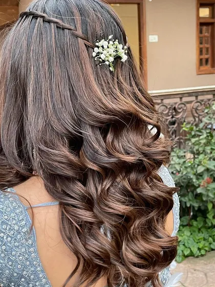 A pretty and cute open hairstyle with soft curls and a simple floral accessory, perfect for a bridesmaid or a pre-wedding event.