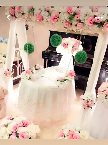 An exquisitely decorated cradle for a naming ceremony. The cradle is draped in white tulle with lace details and surrounded by elegant pink and white roses.