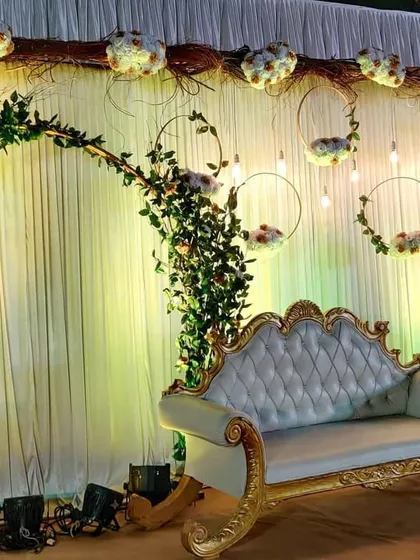 A beautiful stage design featuring a rustic floral arch and hanging floral hoops with light bulbs. The combination of natural elements with elegant lighting creates a unique and romantic backdrop.