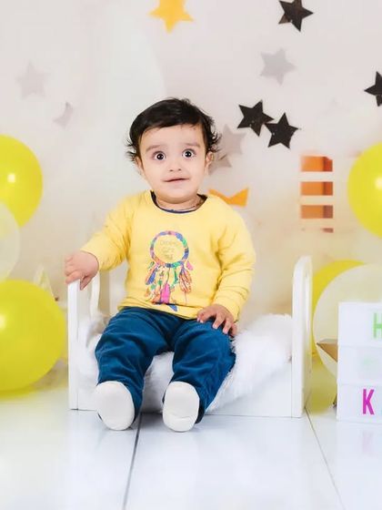 A proud first birthday boy sits on a miniature bed with a "Happy 1st Kabir" sign. A personalized and sweet way to celebrate.