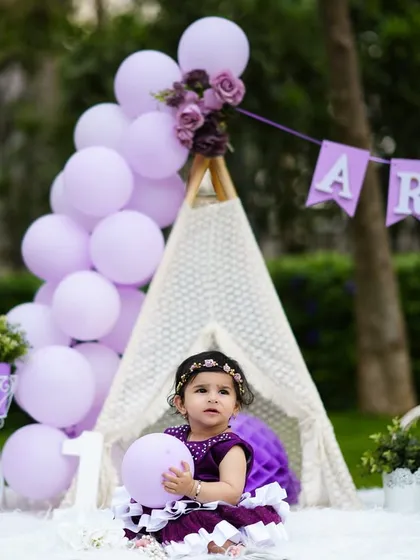 A beautiful outdoor first birthday setup with a teepee and lavender-colored decorations for a baby girl named Arohi.