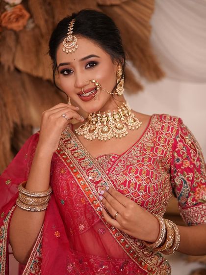 A close-up of a model in a pink and red lehenga, her smile highlighting the beauty of the Kundan choker and nath.