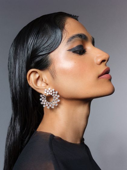 A profile view that provides an excellent look at the intricate design of the diamond cluster earrings. The sleek, wet-look hair styling keeps the focus entirely on the jewelry.