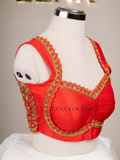 This sleeveless red blouse is perfect for a bold bridal statement. It features a deep V-neckline and is heavily embellished with intricate gold floral zardozi work, creating a rich and luxurious feel.