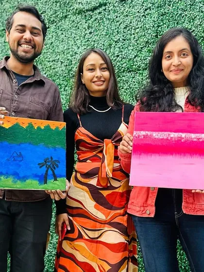 Posing with two happy painters and their finished canvases. One created a vibrant pink abstract piece, while the other painted a serene landscape. It shows how everyone can create something unique even when we start with the same instructions.