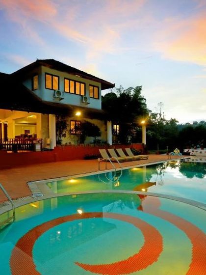 The main building and uniquely designed pool at Riverside Nature Resort, Coorg, illuminated against the twilight sky.