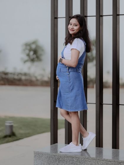 A simple and sweet solo portrait of an expecting mother in a casual denim dress. Her gentle smile and pose highlight the happy and relaxed feeling of her pregnancy.