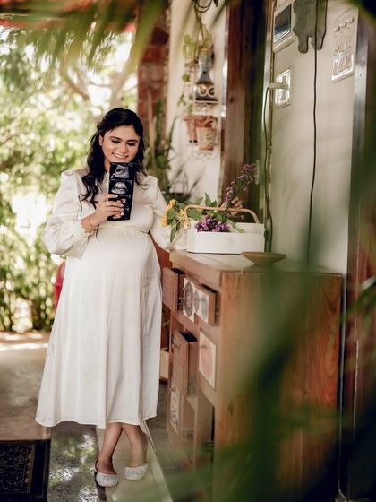 The mom-to-be stands in a beautifully lit indoor space, proudly holding up her sonogram pictures. Her smile reflects the joy of the moment.