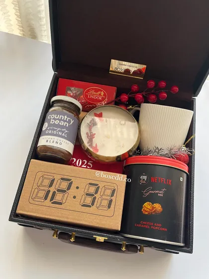 A premium New Year gift packed in a leather-finish trunk. It contains a digital clock, gourmet coffee and popcorn, Lindt chocolate, and a scented candle.