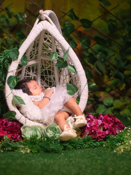 A serene image of a newborn sleeping in a white hanging chair, surrounded by lush greenery and flowers, creating a magical garden scene.